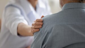 Young woman therapist physician comforting senior aged man at meeting, medical healthcare and help
